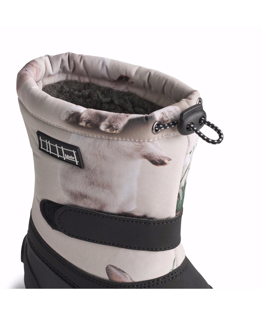 Driven - Winter Rabbits - Praktische Winterstiefel für Kinder mit einer robusten und rutschfesten schwarzen Sohle und einem Druck von niedlichen Kaninchen unter Schneeglöckchen auf grauem Hintergrund.