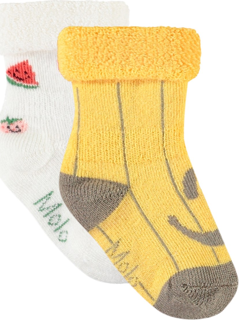Nodda - Little Banana - 2er-Pack Baby-Socken aus Viskose. Die Socken sind weiß mit Früchten und gelb mit lächelnden Gesichtern.
