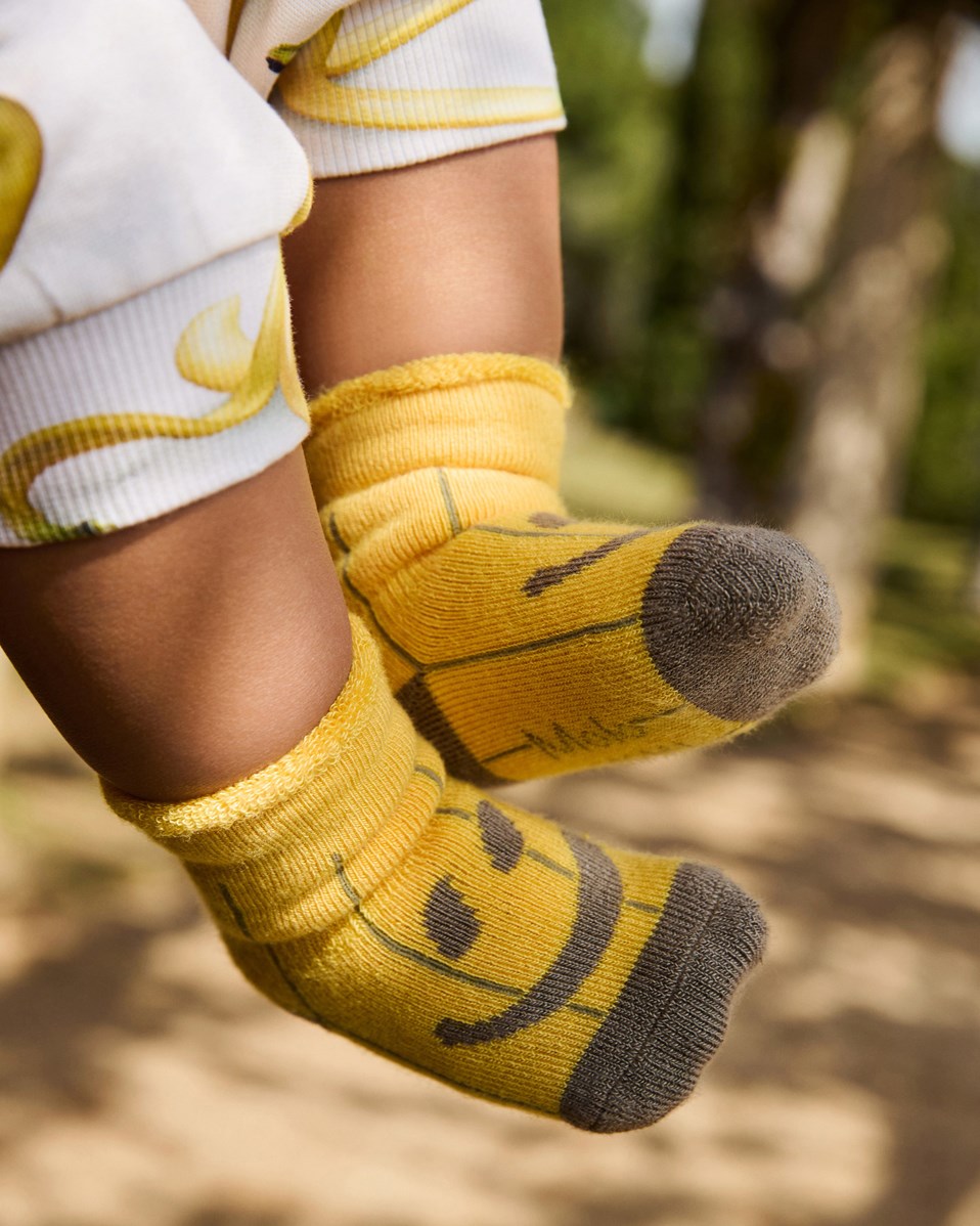 Nodda - Little Banana - 2-pack baby socks in viscose. The socks are white with fruits and yellow with smiling faces.