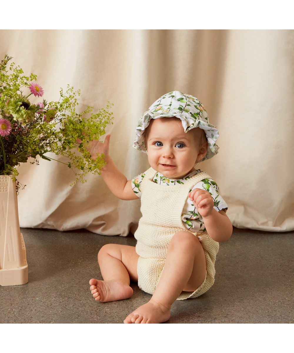 Fleur - Pearled Ivory - Stickad ljusgul babydräkt med axelband.