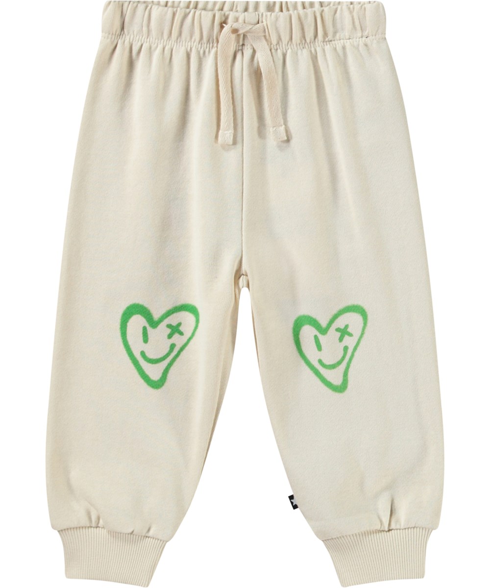 Simeon - Jungle Heart - Mjuka byxor i ekologisk bomull för baby i ljusbeige med leende hjärta.