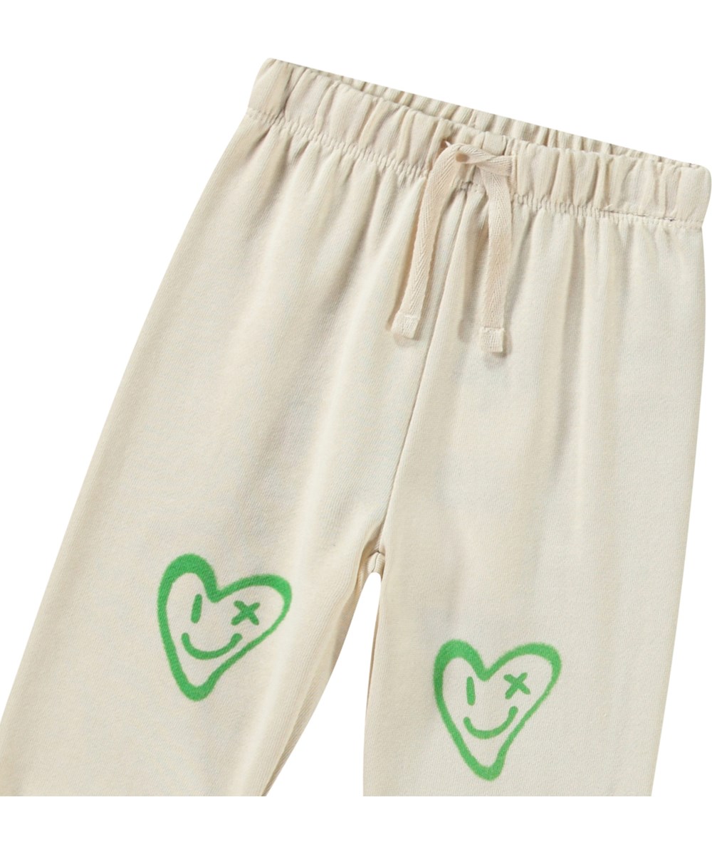 Simeon - Jungle Heart - Mjuka byxor i ekologisk bomull för baby i ljusbeige med leende hjärta.