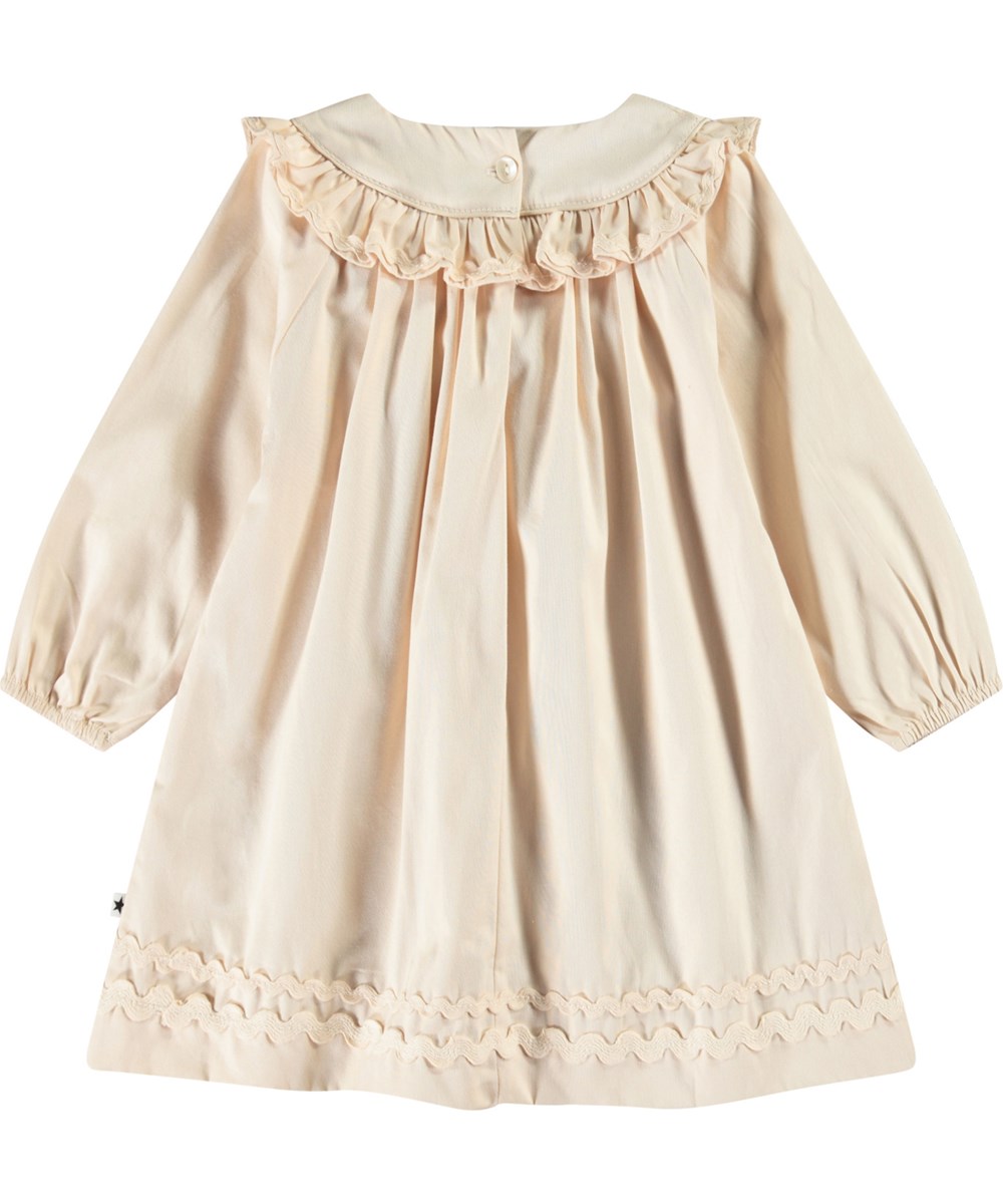 Cailin - Brazilian Sand - Beige babyklänning i ekologisk bomull med volangdetaljer.
