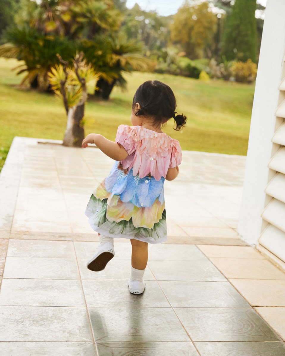 Caja - Petal Rainbow - Poplindress i ekologisk bomull för baby med rymlig passform. Klänningen är mångfärgad med fjädrar och blomblad.
