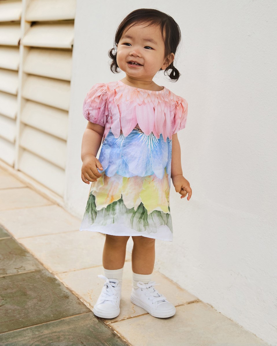 Caja - Petal Rainbow - Popelinekleid aus Öko-Baumwolle für Babys. Weite Passform. Das Kleid ist mehrfarbig mit einem Druck von Federn und Blütenblättern.