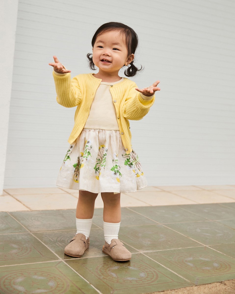 Candi - Baby Dandelion - Langärmeliges Kleid für Babys aus Öko-Baumwolle. Das Kleid ist gelb mit einem Löwenzahn-Druck.