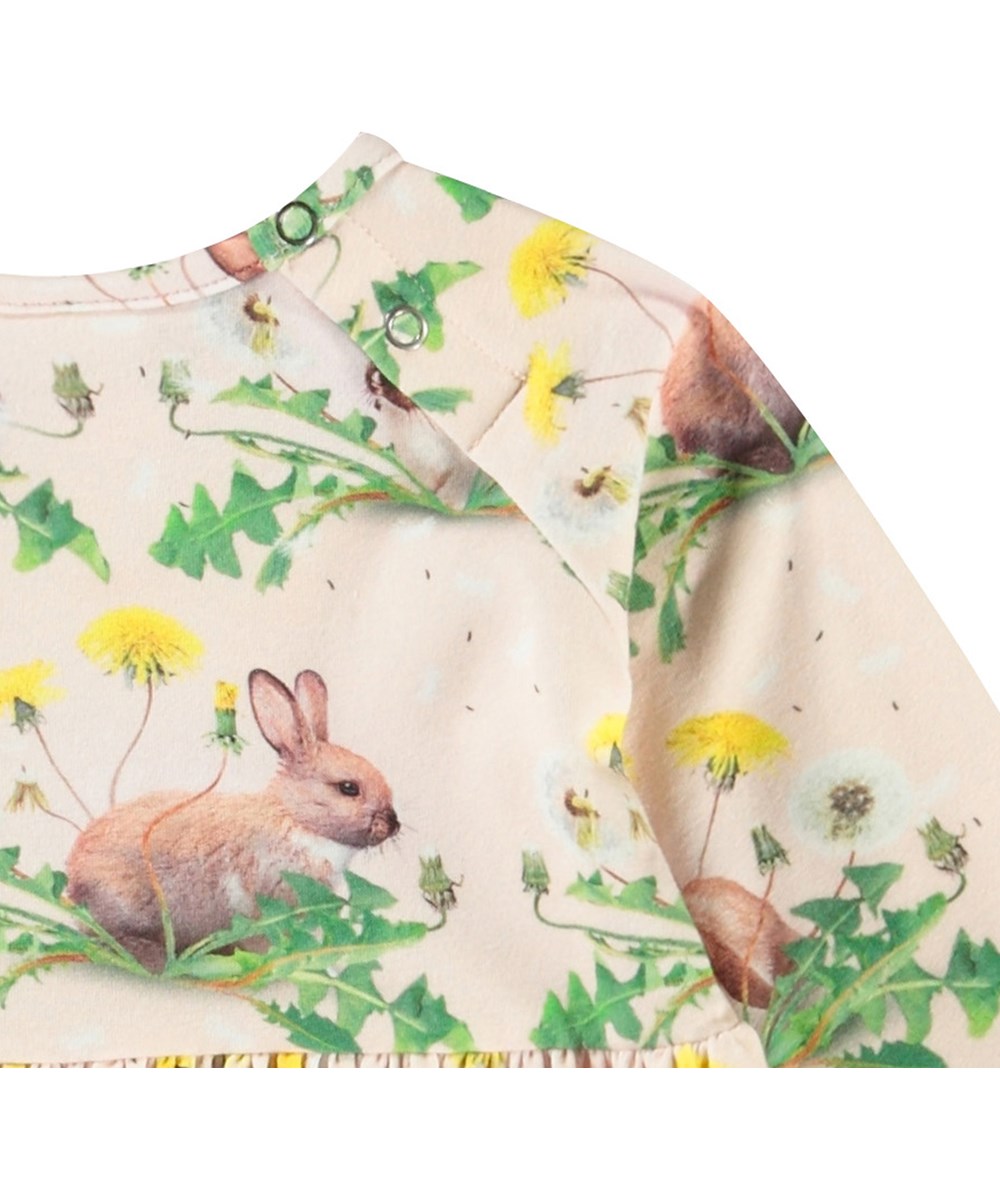 Charmaine - Bunnies United - Langärmeliges Kleid für Babys aus Öko-Baumwolle. Das Kleid hat einen Aufdruck von Hasen und Löwenzahn.