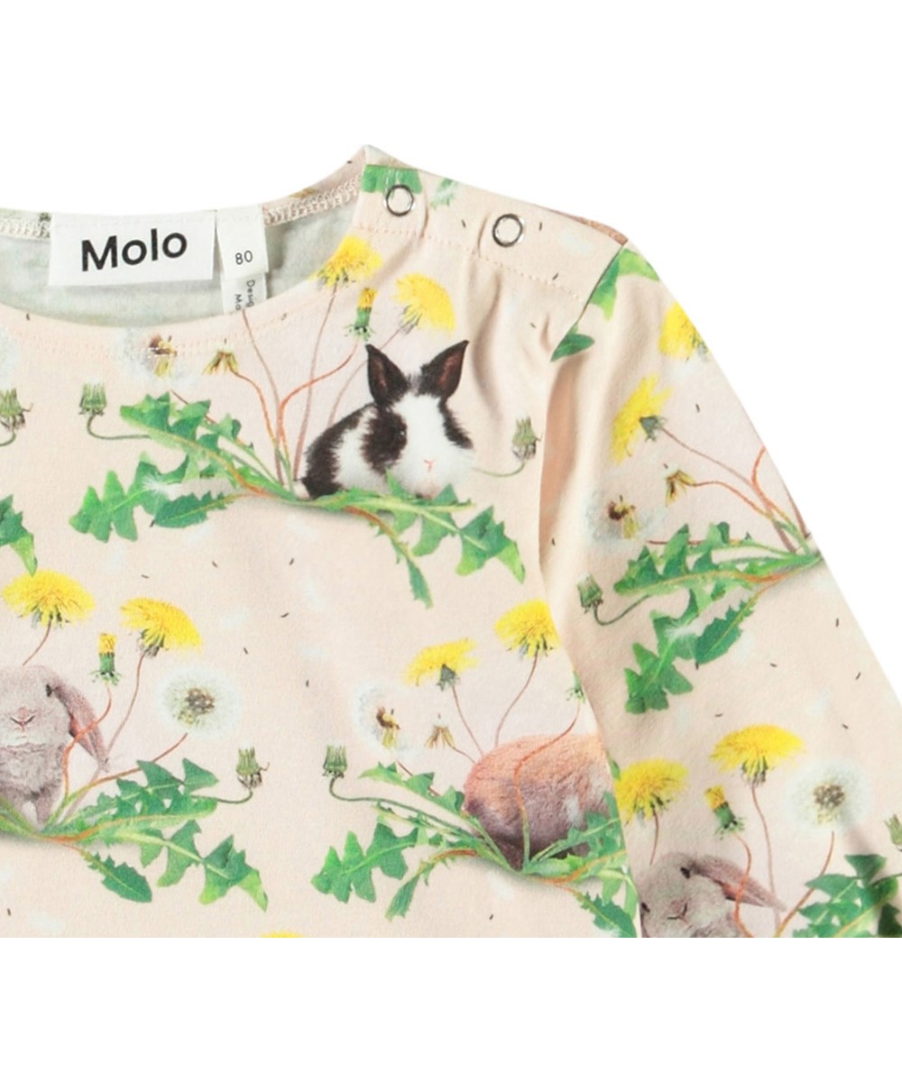 Elina - Bunnies United - Langärmeliges Oberteil aus Öko-Baumwolle für Babys. Die Bluse ist rosa mit einem Aufdruck von Hasen und Löwenzahn.