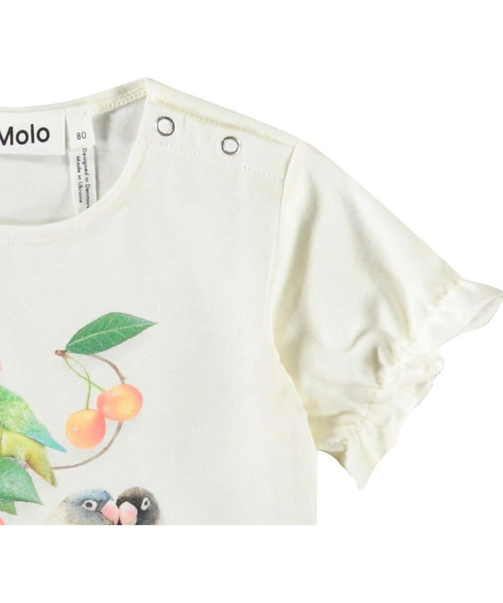 Eline - Love Birds - T-Shirt mit Rüschen-Details aus Öko-Baumwolle für Babys. Weiß mit einem Frontdruck von kleinen Papageien und Kirschen.