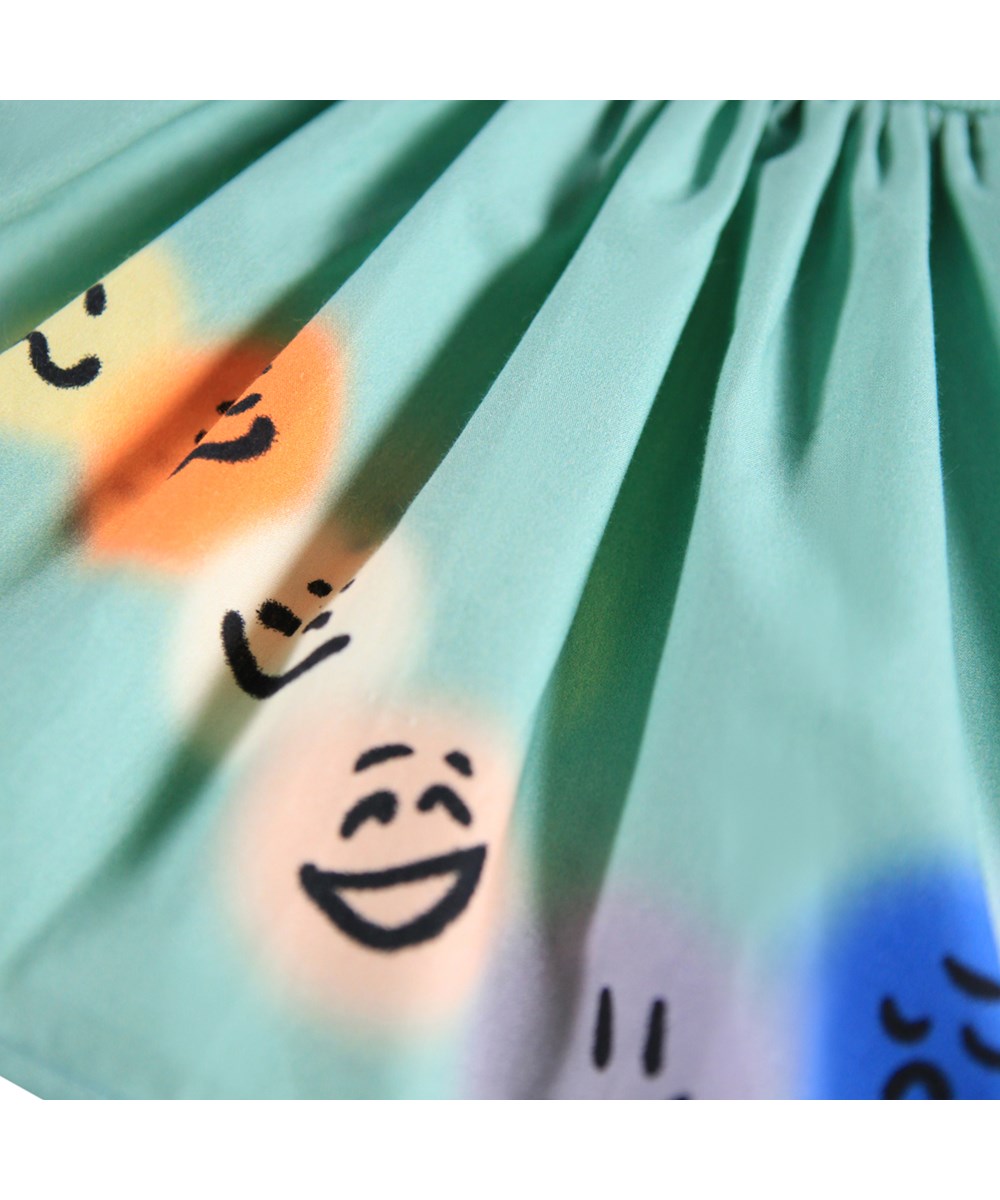 Caitlin - Wavy Moods - Groene popeline jurk voor de kleintjes gemaakt van biologisch katoen met een print van gezichten in verschillende stemmingen.