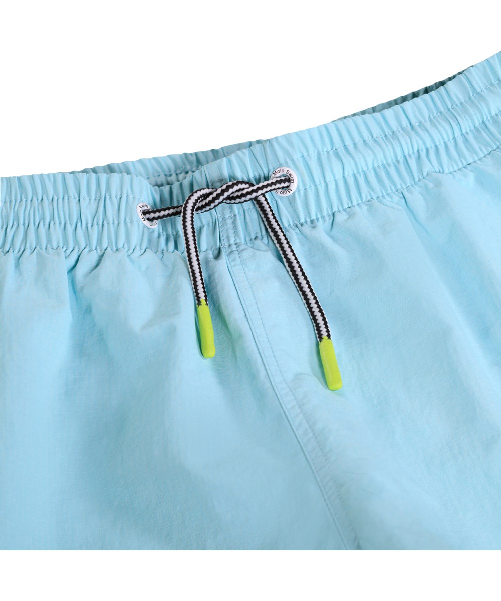 Niko Solid - Blue Light - Blaue, sportliche Badeshorts für Kinder aus recyceltem Nylon mit UV-Schutz 50+.