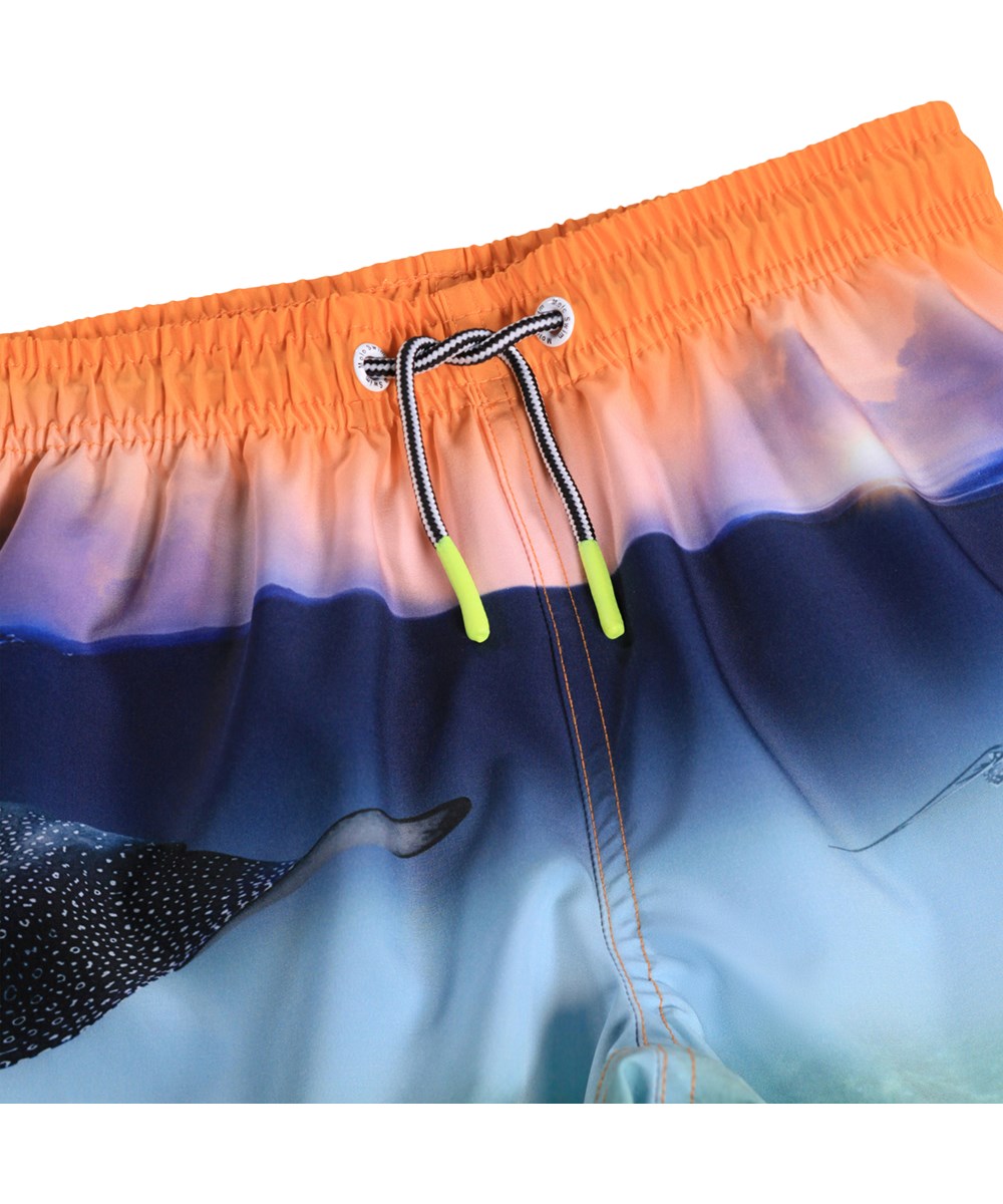 Niko - Into The Sunset - Sportiga badshorts i blått och orange med havsmönster för aktiva barn i återvunnen polyester med UV-skydd 50+.
