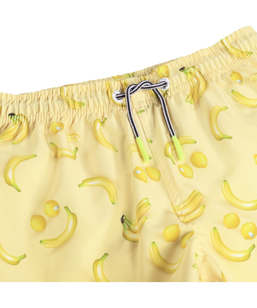 Niko - Lemon Banana - Sportiga, gula badshorts med fruktmönster för aktiva barn i återvunnen polyester med UV-skydd 50+.