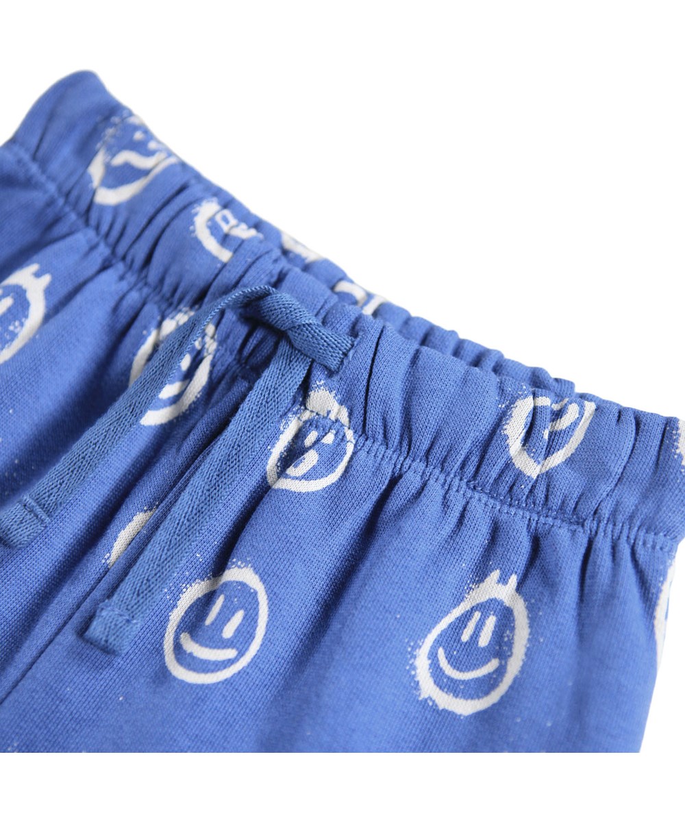 Simeon - Blue Moods - Mjuka blå byxor för baby i ekologisk bomull med vita ansikten i olika humör.