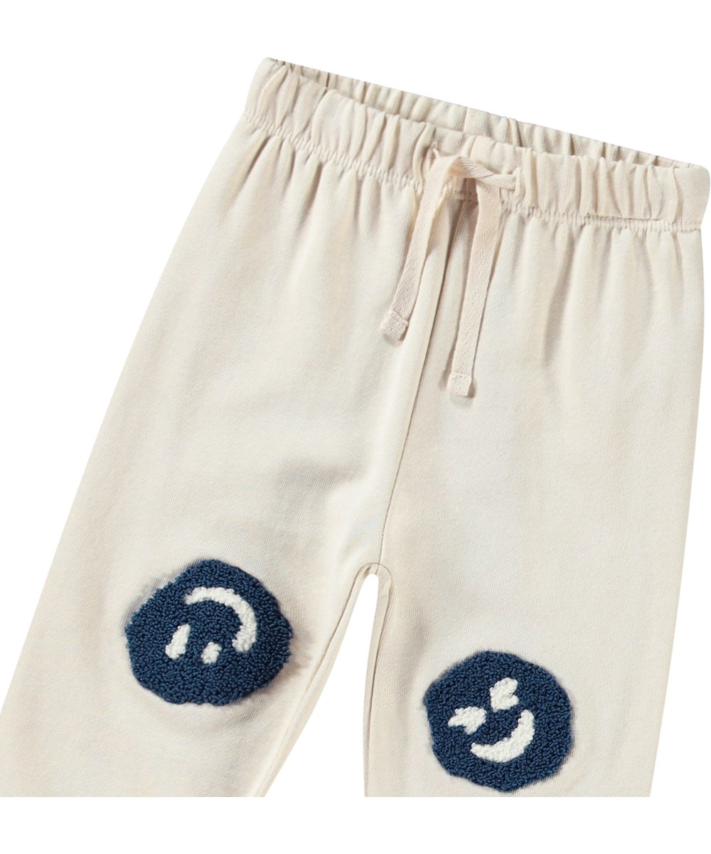 Simeon - Summer Sand - Mjuka byxor i ekologisk bomull för baby. Byxorna är ljusbeige med mjuka smileys.