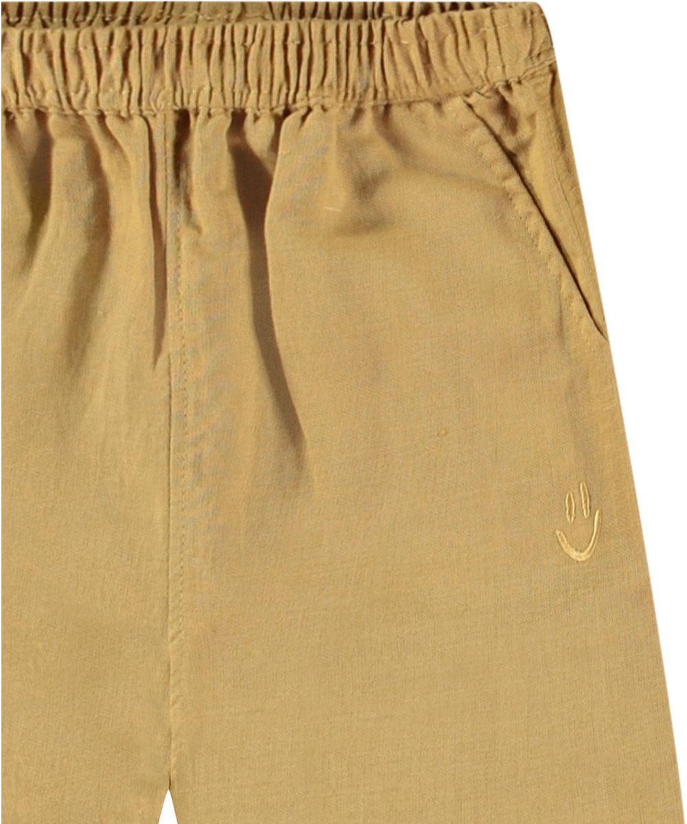 Sois - Suede - Byxor i ekologisk bomull för baby. Byxorna är bruna med en liten broderad smiley vid fickan.