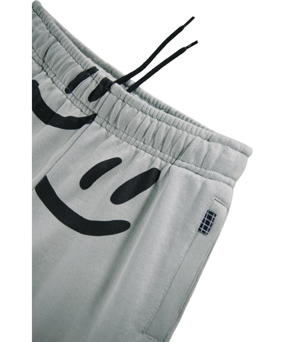 Adan - Big Smiles Fall - Grijze joggingbroek voor kinderen gemaakt van biologisch katoen met een print van lachende gezichten.