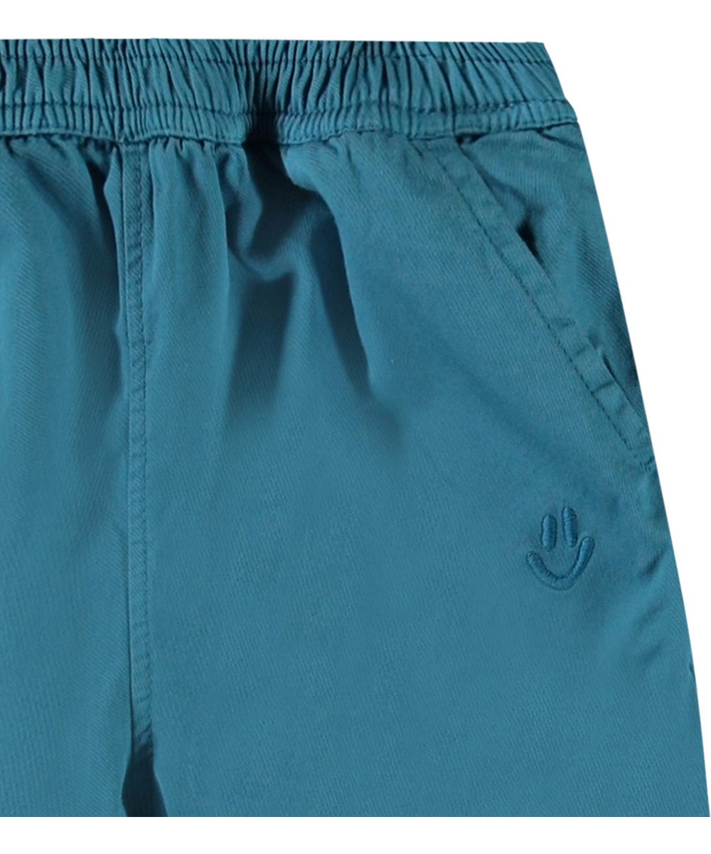 Sois - Lagoa - Babybroek van biologisch katoen. De broek is blauw met een klein geborduurde smiley bij de zak.