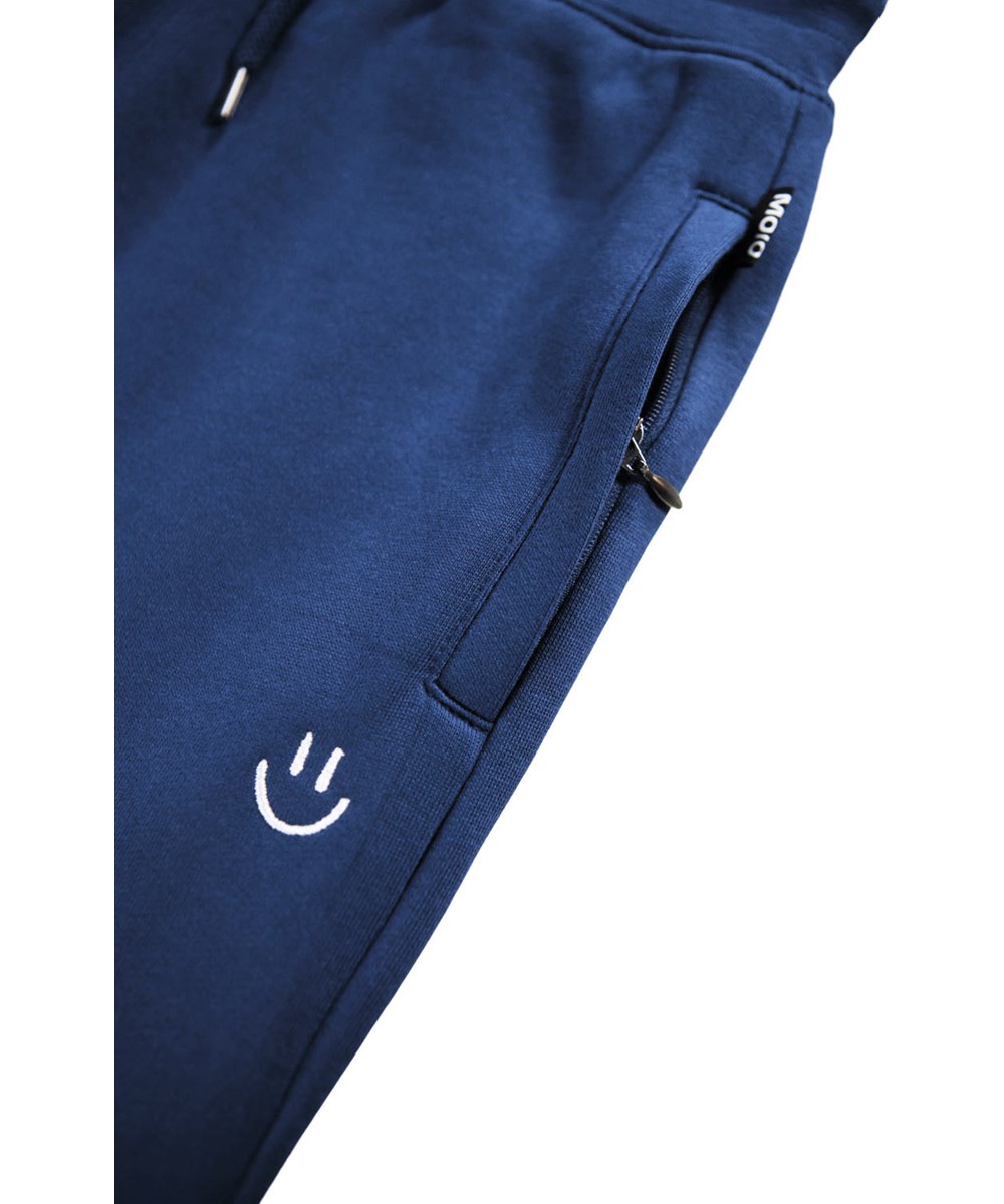 Alvar - Blue Depths - Blå sweatpants i økologisk bomuld med broderet hvidt smilende ansigt.