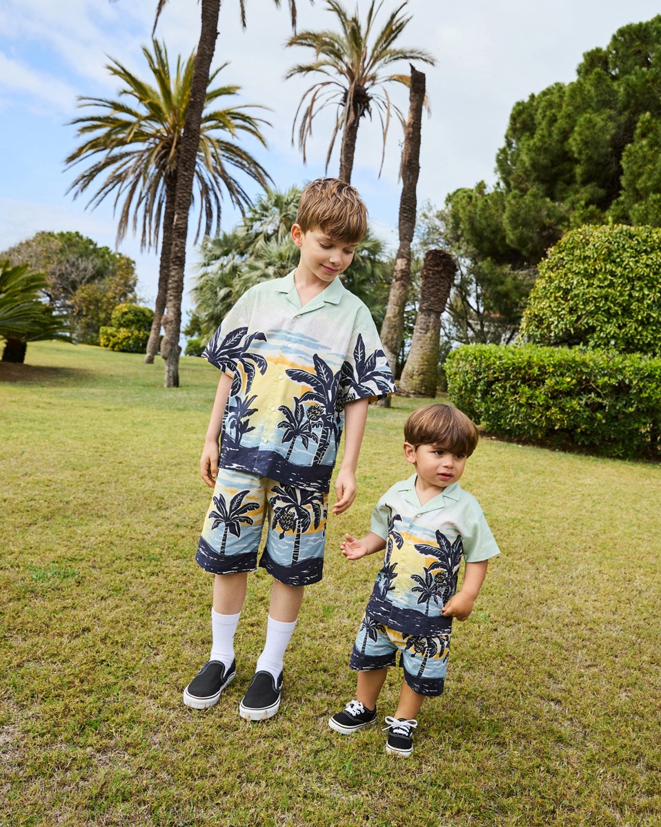 Eyou - Babynanas Palm - Kurzarmshirt aus Öko-Baumwolle für ein Baby. Das Shirt ist hellgrün mit einem Aufdruck von Palmen und einem Sonnenuntergang.