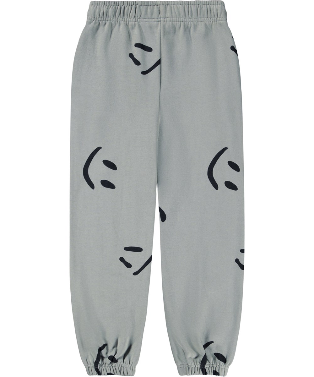 Adan - Big Smiles Fall - Graue Jogginghose für Kinder aus Öko-Baumwolle mit einem Aufdruck von lächelnden Gesichtern.