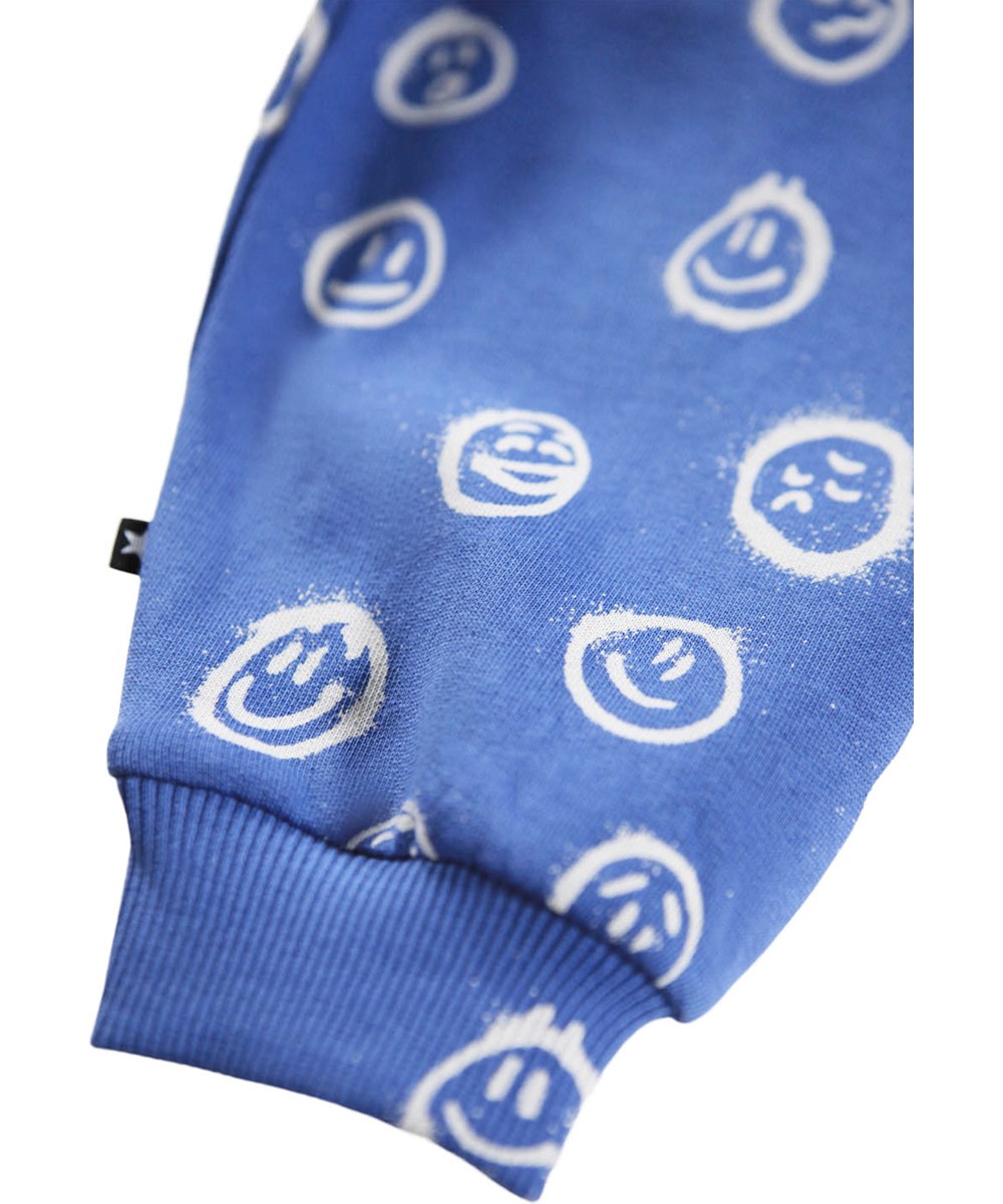 Simeon - Blue Moods - Weiche blaue Hosen für die Kleinen aus Öko-Baumwolle mit einem Aufdruck von weißen Gesichtern in verschiedenen Stimmungen.