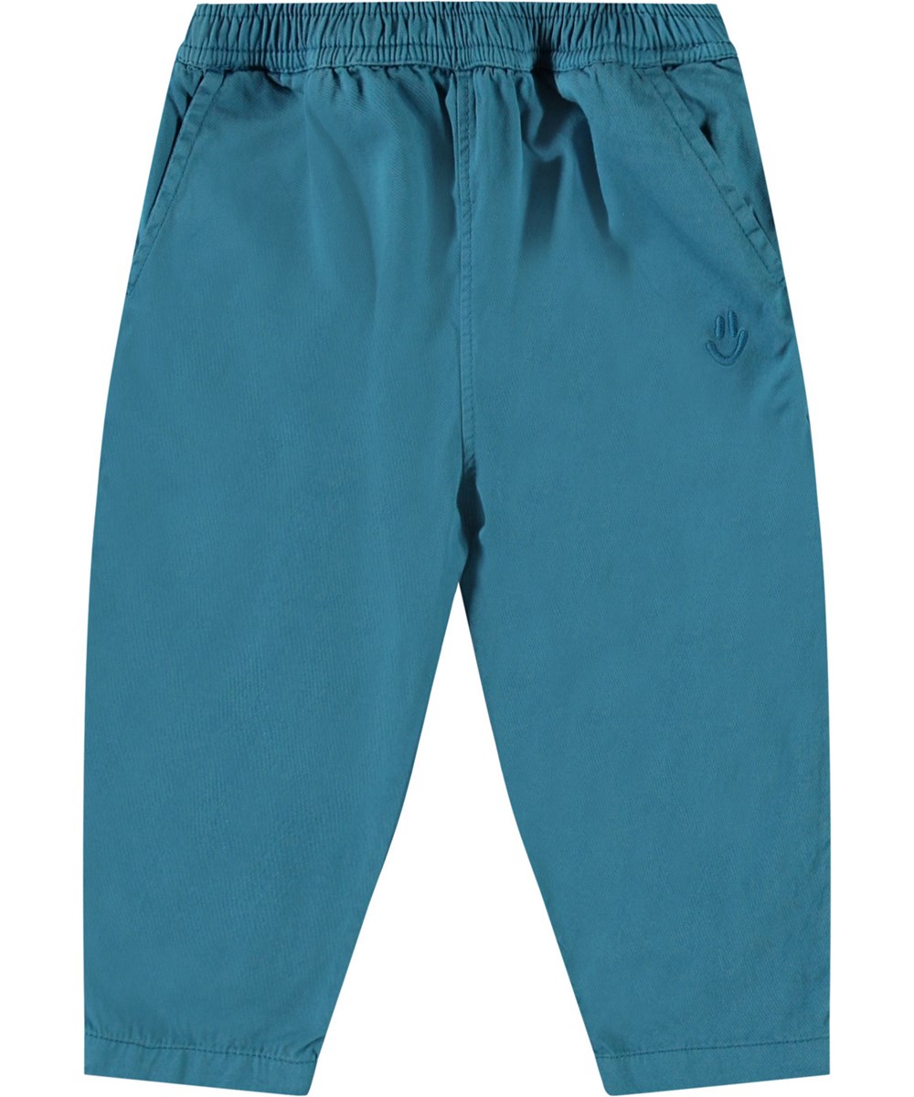 Sois - Lagoa - Hose aus Öko-Baumwolle für Babys. Die Hose ist blau mit einem kleinen gestickten lächelnden Gesicht an der Tasche.