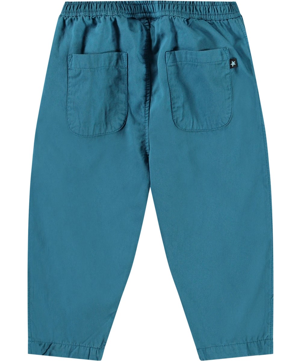 Sois - Lagoa - Hose aus Öko-Baumwolle für Babys. Die Hose ist blau mit einem kleinen gestickten lächelnden Gesicht an der Tasche.