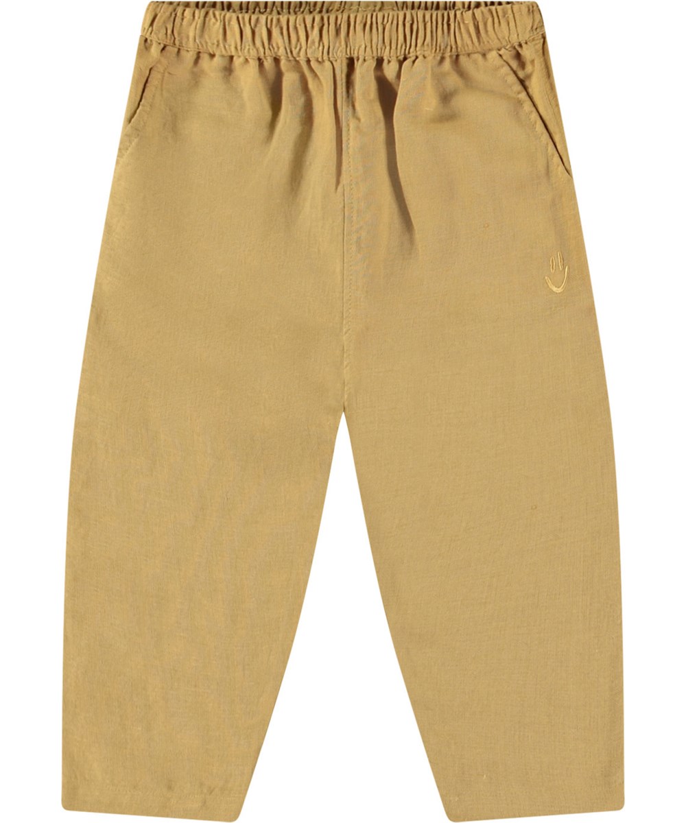 Sois - Suede - Hose aus Öko-Baumwolle für Babys. Die Hose ist braun mit einem kleinen gestickten lächelnden Gesicht an der Tasche.