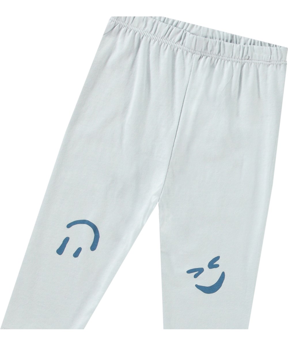 Simway - Skywriting - Pants in organic cotton jersey for baby. It has a close-fitting with elastic waist. The trousers are light blue with a print of smiling faces on the knees.