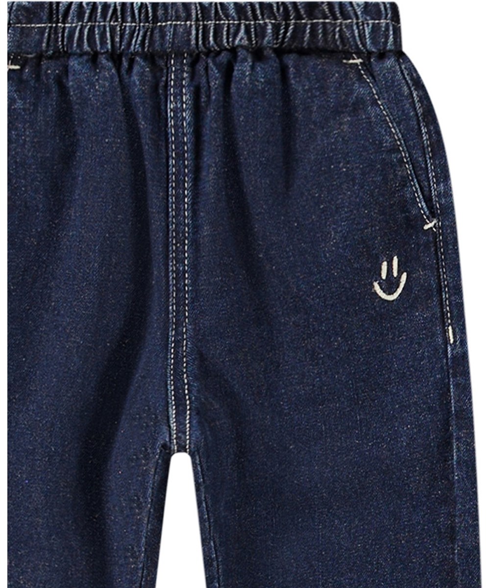 Sois - Oceanic Denim - Blue denim trousers for kids with loose fit, elastic waist, and pockets. Lightweight and airy with embroidered smiling face.