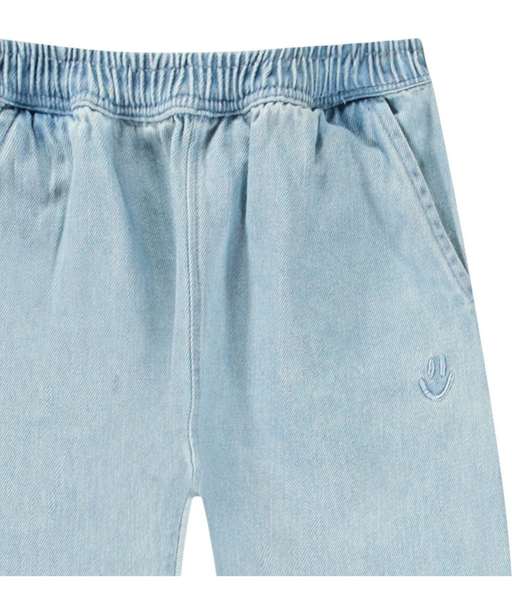 Sois - Misty Denim - Pants in organic cotton for baby. In blue denim with embroidered smiling face by the pocket.