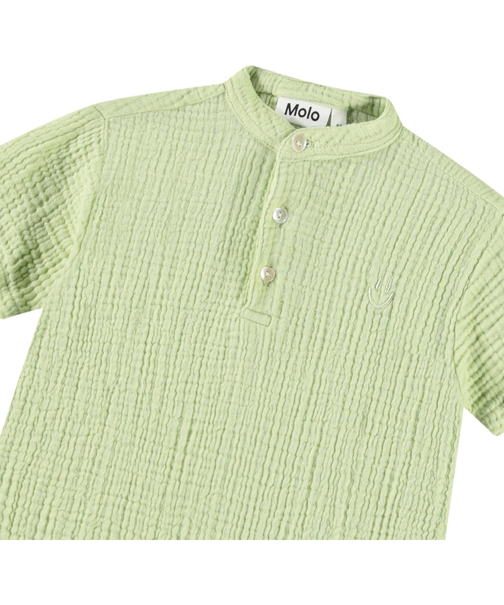 Ever - Misty Green - Short-sleeved shirt with buttons in organic crinkled cotton for a baby. The shirt is light green with a small embroidered smiling face.