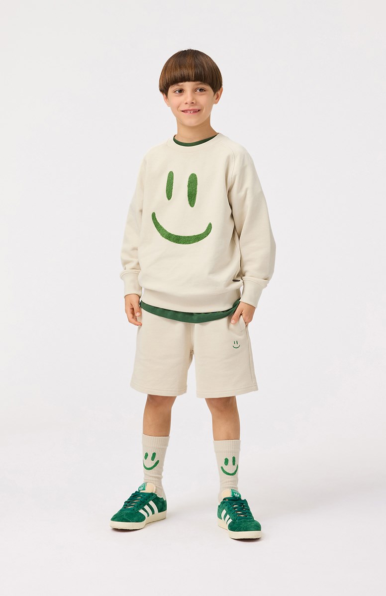 Alw - White Noise - Beige Shorts aus Öko-Baumwolle mit einem grünen lächelnden Gesicht für Kinder.