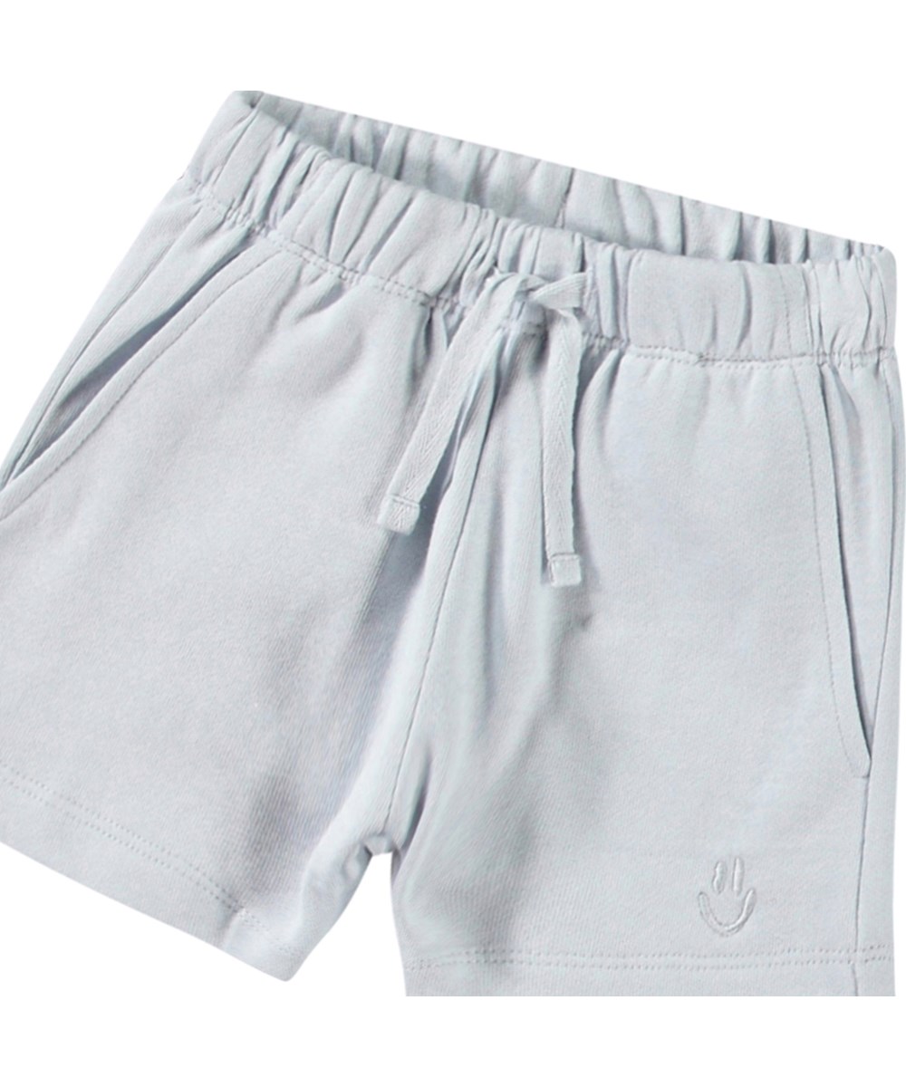 Simms - Skywriting - Soft shorts in organic cotton for baby. These shorts are light blue with an embroidered smiling face on one leg.