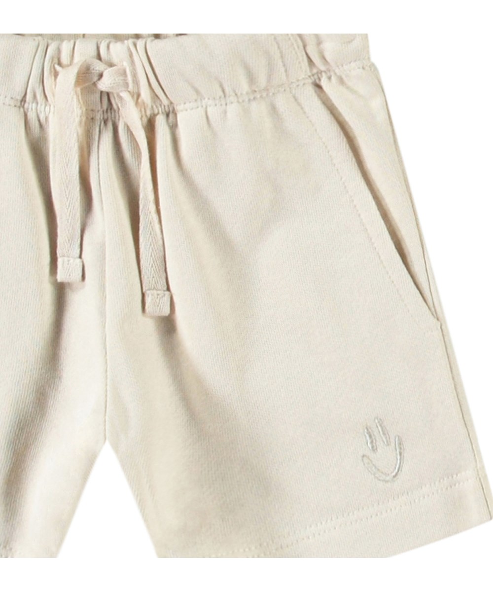 Simms - Summer Sand - Soft shorts in organic cotton for baby. These shorts are light beige with an embroidered smiling face.