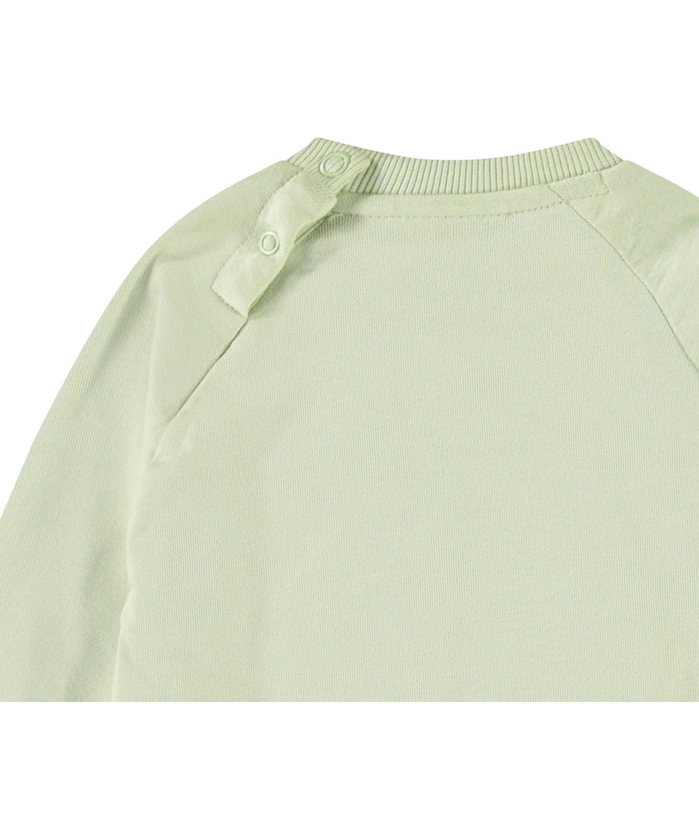 Disc - Misty Green - Organic light green baby sweatshirt with a soft smiling face.