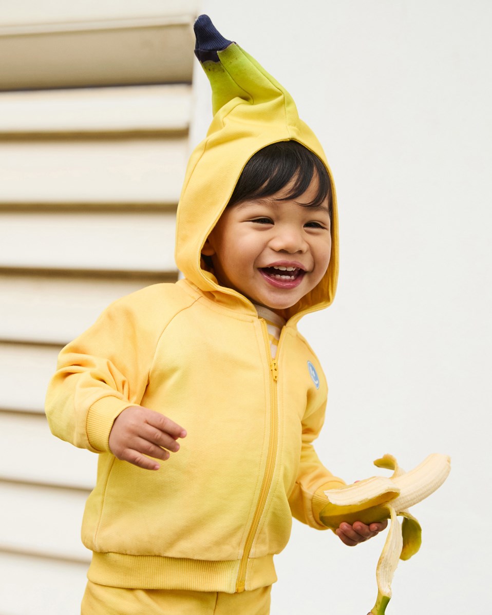 Dani -  Be A Banana - Kapuzenpullover aus Öko-Baumwolle für Babys. Der Kapuzenpullover ist gelb mit Bananen-Details.