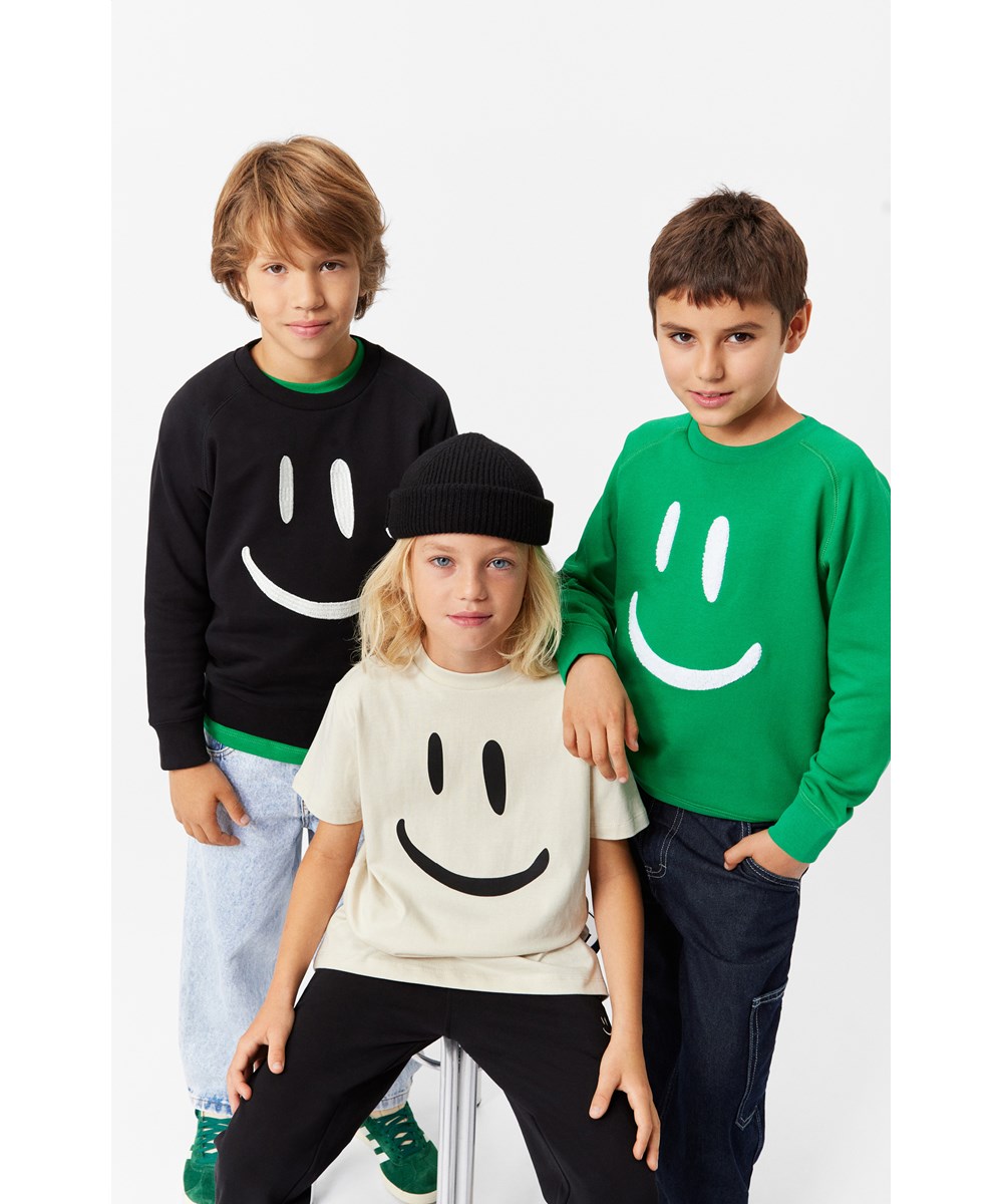 Mike - Black - Molo x Plan International Öko-Baumwoll-Sweatshirt in Schwarz mit einem aufgestickten Lächeln auf der Vorderseite.