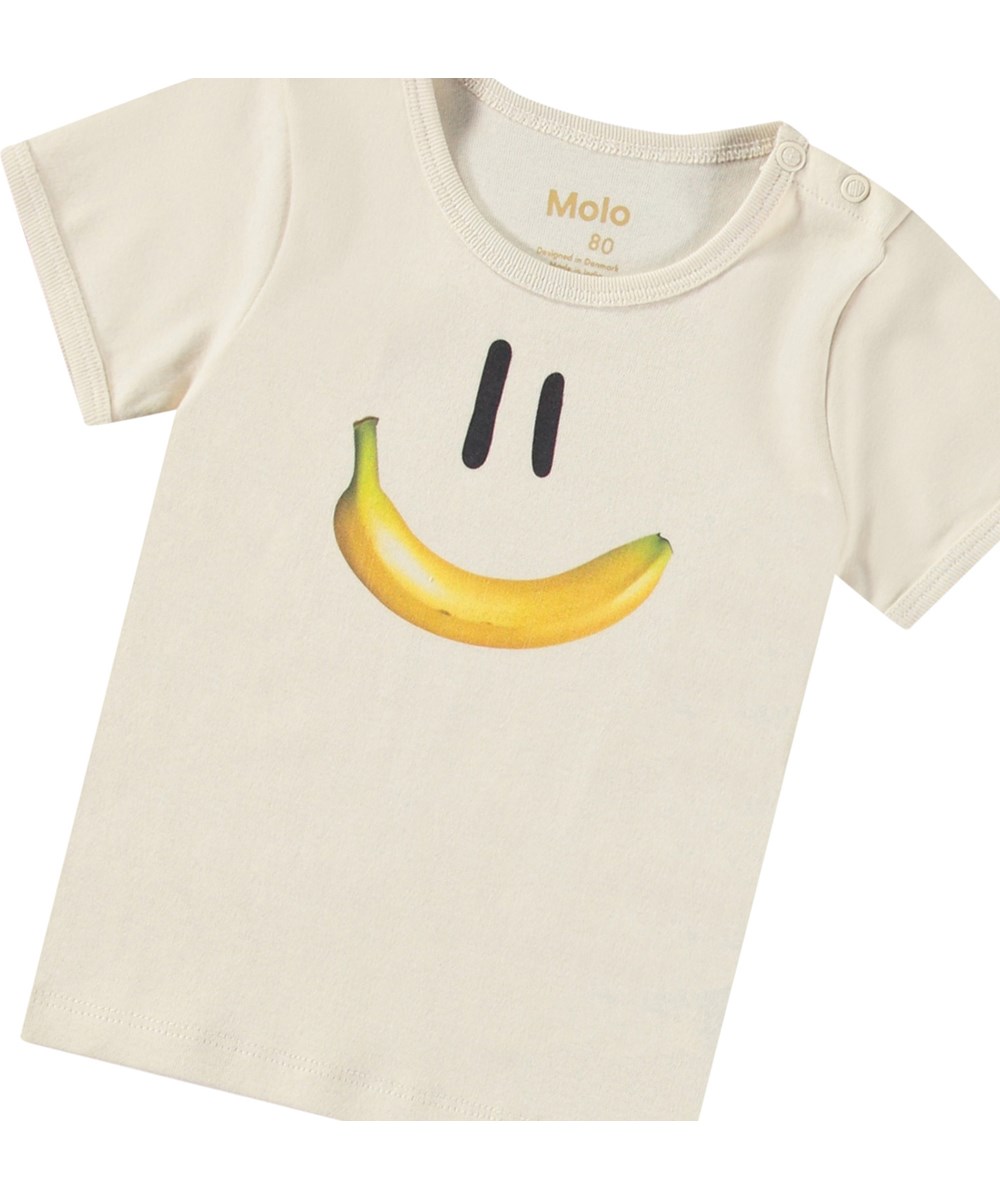 Easy - Babynanas Smile - Beiges Öko-Baumwoll-T-Shirt für Babys. Das T-Shirt hat eine enge Passform und zeigt ein lächelndes Gesicht mit einem Bananenmund.
