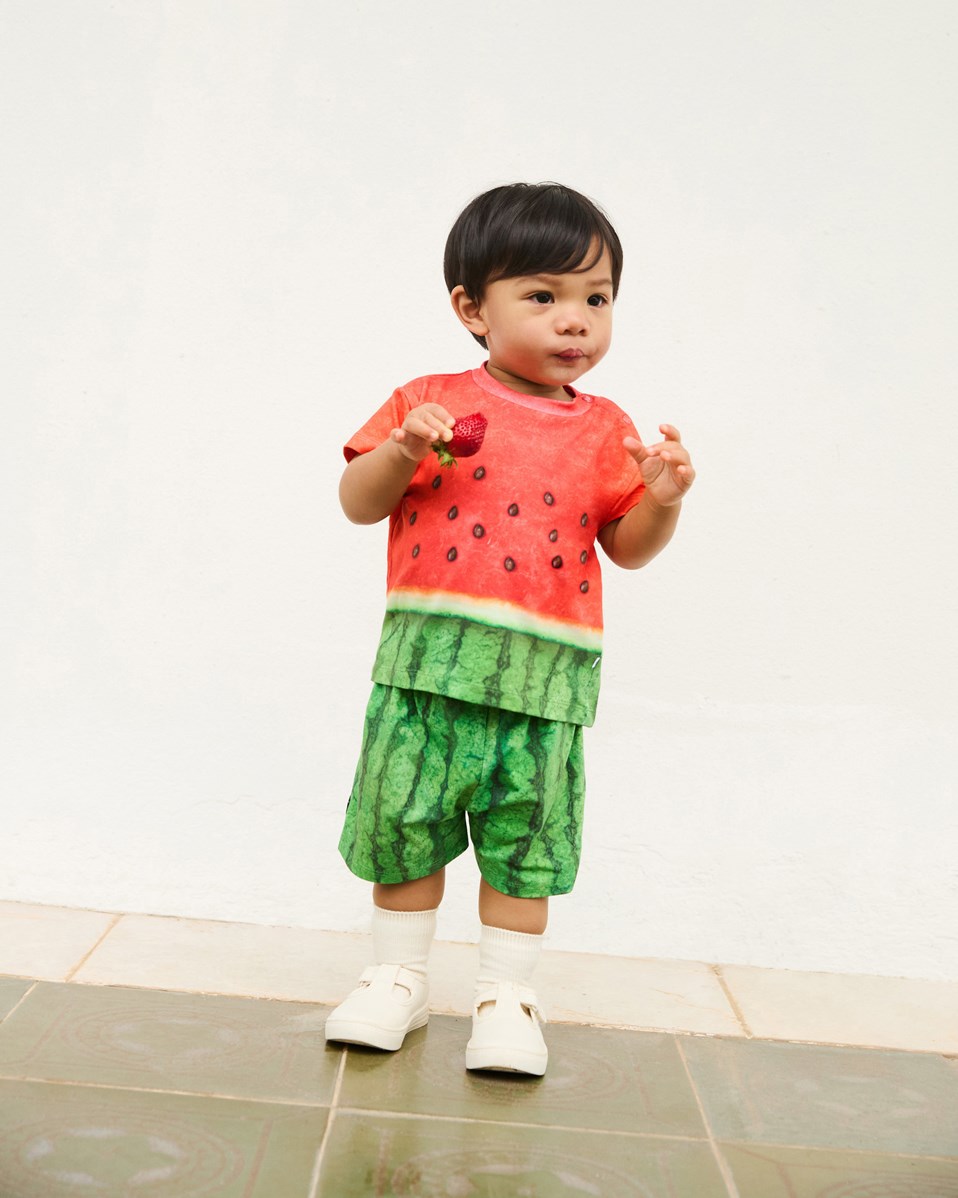Enzo - Be A Melon - Klassisches Öko-Baumwoll-T-Shirt für Babys. Das T-Shirt ist mit einem Wassermelonen-Druck in Grün und Rot versehen.