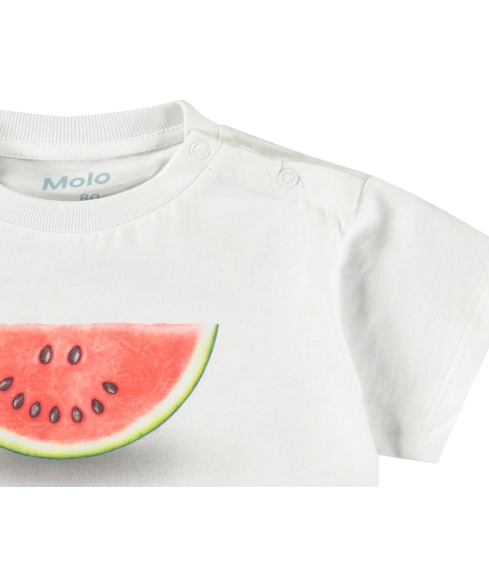 Enzo - Melon Smile - Klassisches Öko-Baumwoll-T-Shirt für Babys. Das T-Shirt ist weiß mit einem Frontdruck einer lächelnden Wassermelonen-Scheibe.