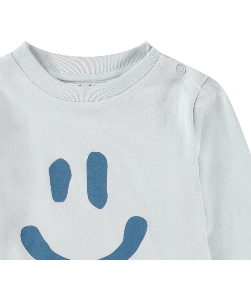 Eloy - Skywriting - Økologisk baby bluse med et print af et smilende ansigt.