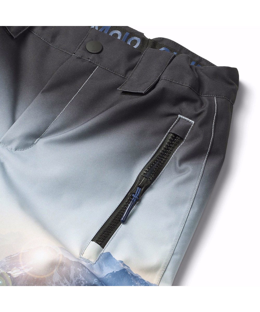 Jump Pro - High In Sky - Wind- en waterdichte skibroek voor kinderen van gerecycled polyester met een print van de besneeuwde Alpen met zonnestralen en een helderblauwe lucht.