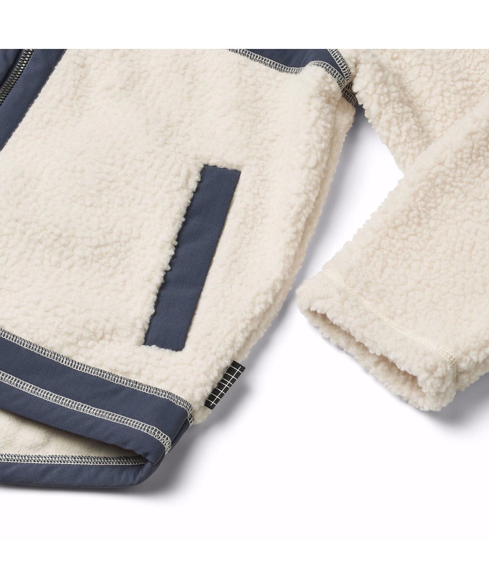 Usher - Summer Sand - Gebroken witte fleece jas voor kinderen van gerecycled polyester met voorzakken en blauwe duurzame details.