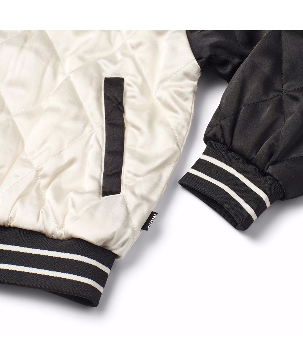 Haru - Molo-Cross - Doorgestikte bomberjacket voor kinderen in de kleuren zwart en gebroken wit met op de achterkant een geborduurde motorcrosser en de tekst 'Courage'.