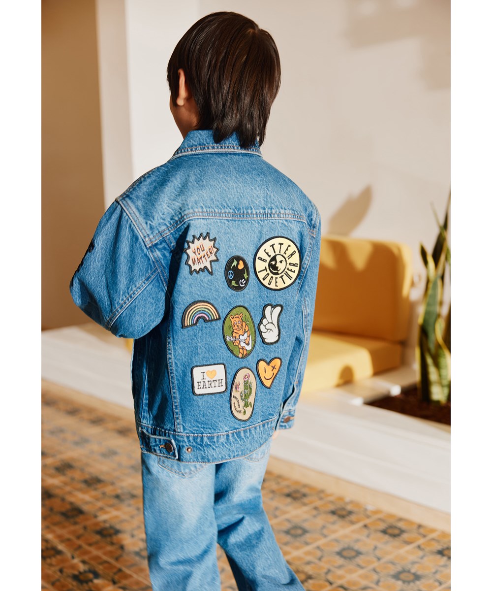 Honore - True Blue - Blauw spijkerjack voor kinderen gemaakt van katoen met kleurrijke geborduurde patches op de achterkant.