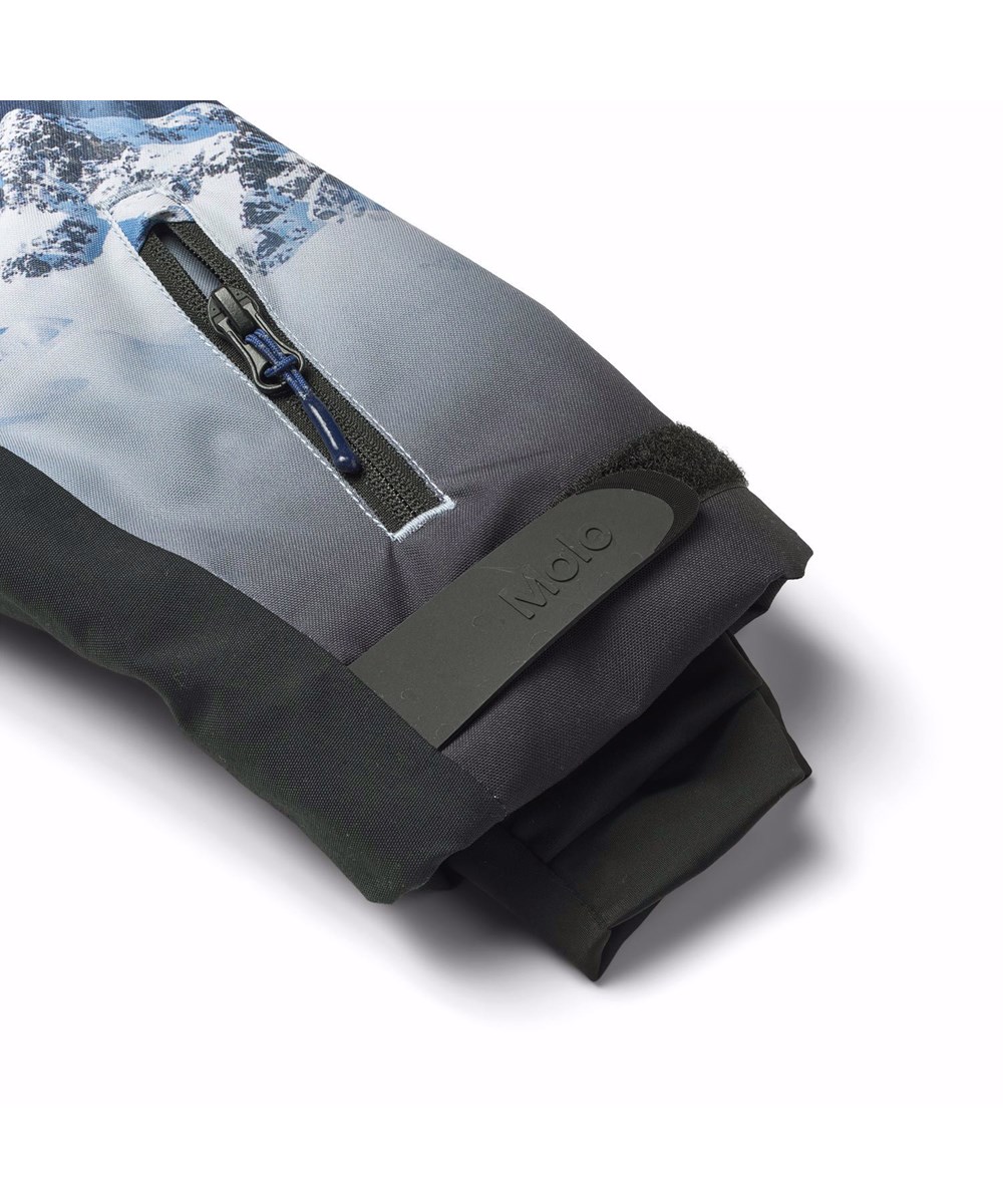 Alpine - High In Sky - Wind- en waterdichte ski-jas voor kinderen van gerecycled polyester met een print van de besneeuwde Alpen met zonnestralen en een heldere lucht.