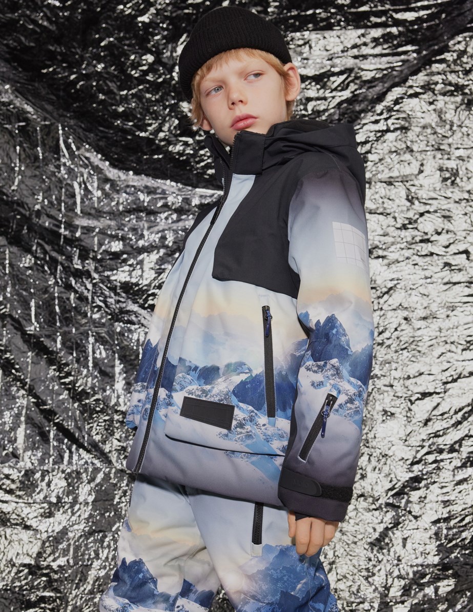 Alpine - High In Sky - Wind- en waterdichte ski-jas voor kinderen van gerecycled polyester met een print van de besneeuwde Alpen met zonnestralen en een heldere lucht.