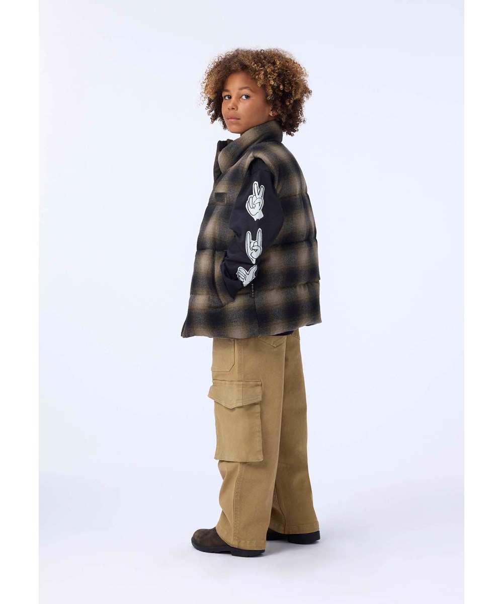 Heike - Bark Check - Geruite bruine gewatteerde kinderbodywarmer gemaakt van gerecycled polyester en wolmix met interne verstelbare elastische banden die de wind buiten houden.